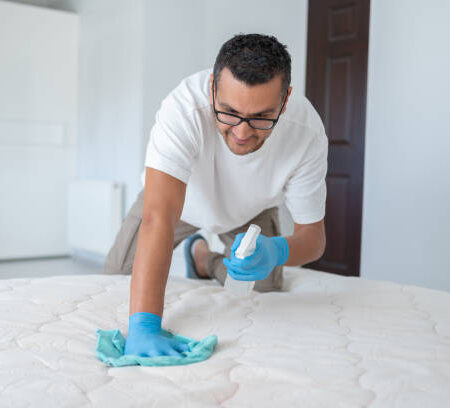 f8 Man Hands In Rubber Protective Glove With Micro Fiber Cloth And Detergent Spray Bottle Cleaning A Mattress Cloth With A Liquid Stain Remover In Bedroom At Home