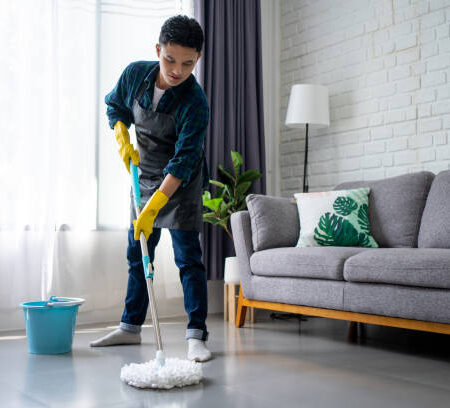 h4 Handsome asian man wearing apron cleaning floor at home. Guy washing floor with mopping stick and bucket in living room.