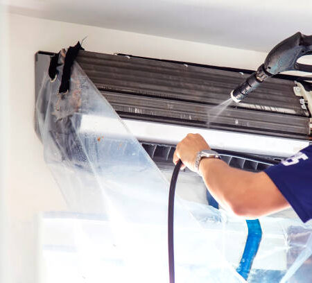 h5 The technicians are cleaning the air conditioner by spraying water. Hand and water spray are cleaning the air conditioner on white background.