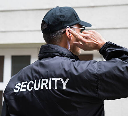 Rear view of mature security guard listening to earpiece against building Rear view of mature security guard listening to earpiece against building